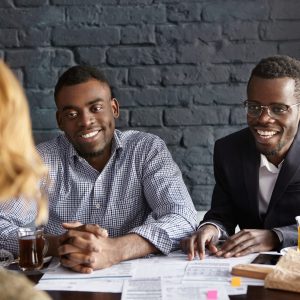 Unrecognizable female with shirt hairstyle is about to be hired for desired position in large company by two cheerful dark-skinned handsome recruiting experts, laughing happily during job interview